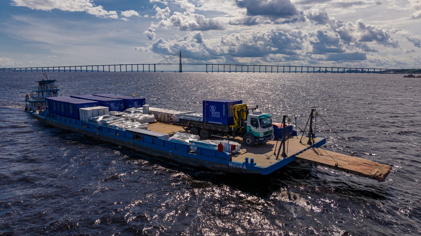 Balsa levando contêineres Norte Conectado pelo Rio Negro, com a ponte de Manaus ao fundo
